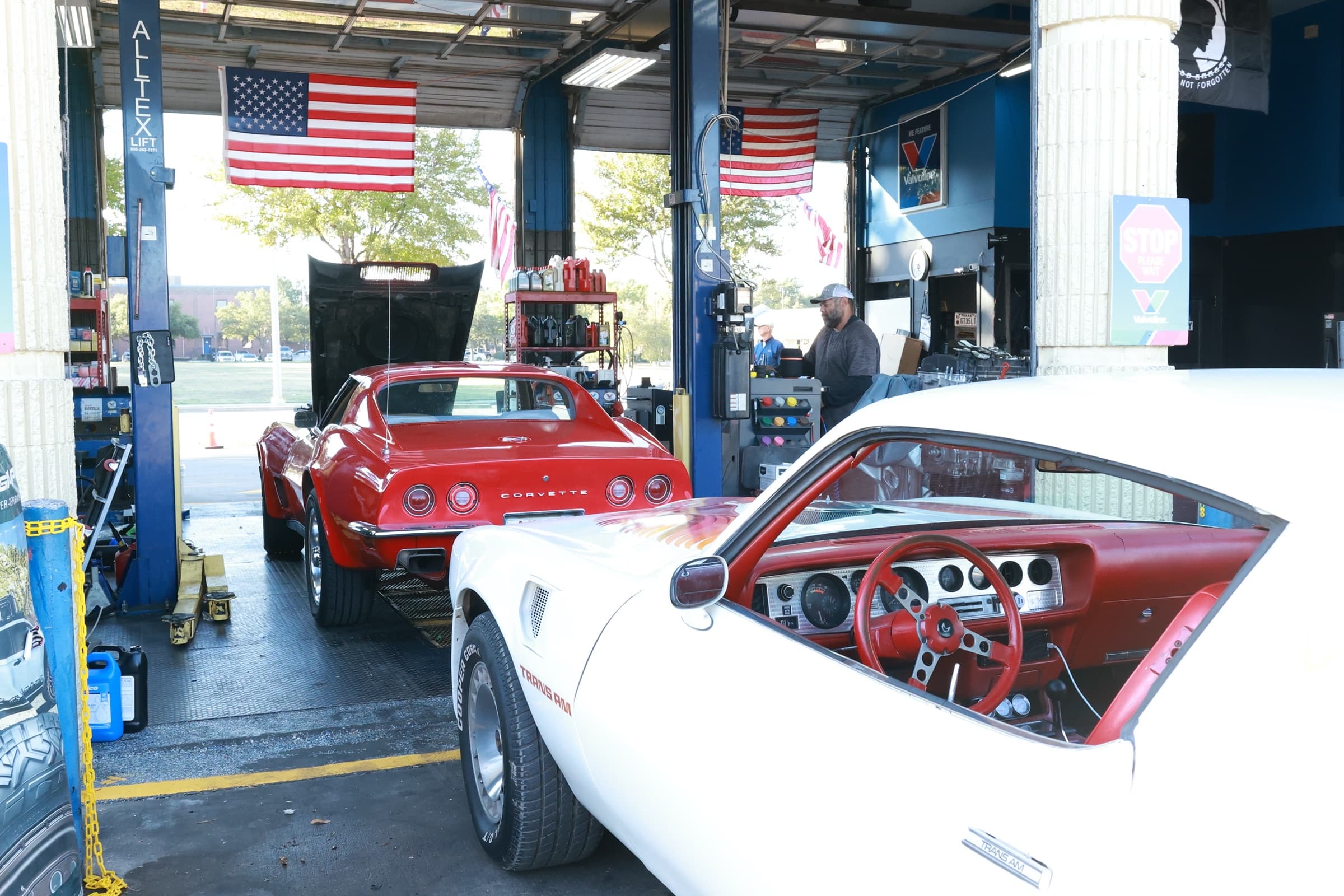 Service bay with classic American cars, lifts, and flags at Patriot Auto Repair